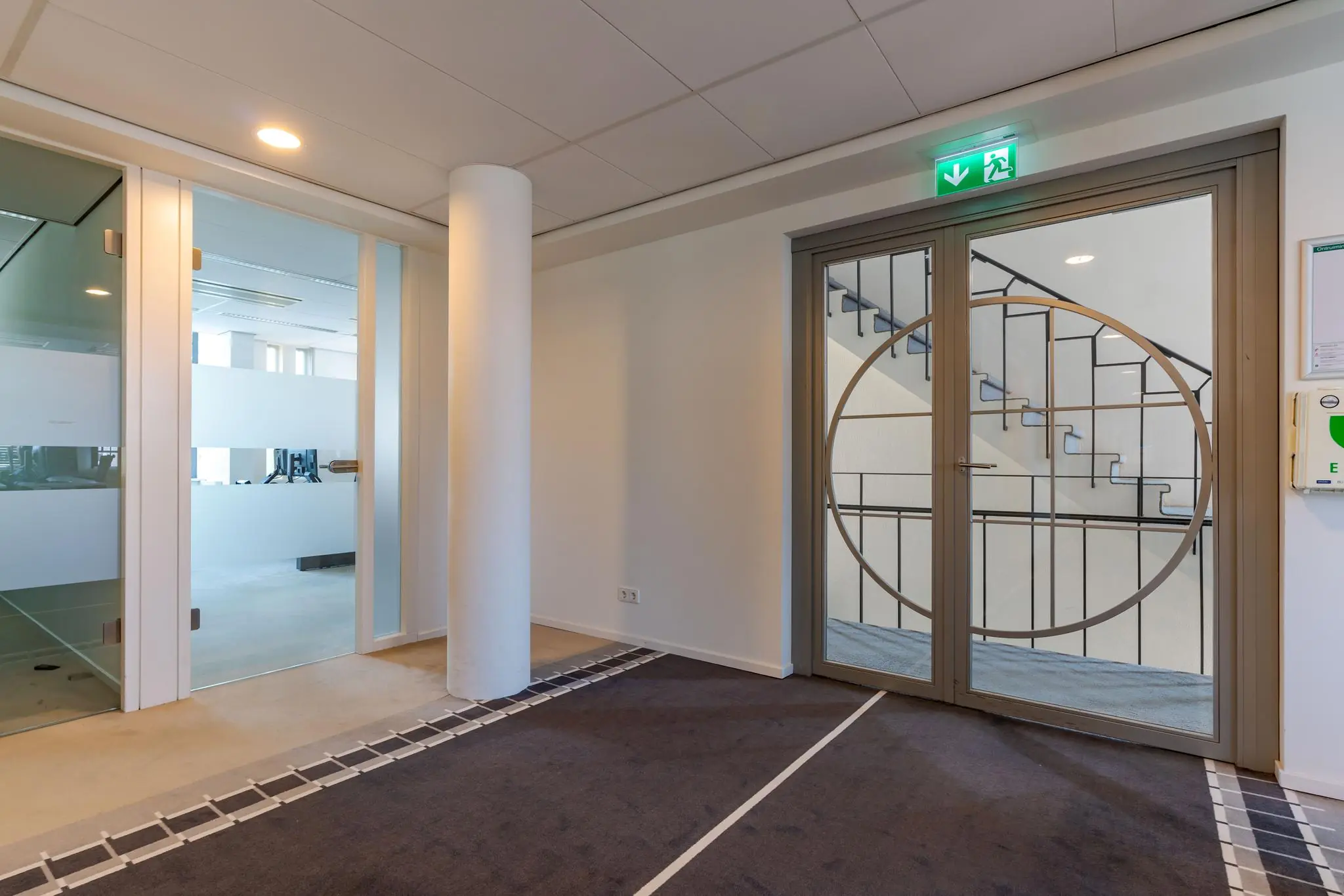 Moderne kantoorhal met glazen deuren en zicht op een trapportaal aan de Van Alkemadelaan.